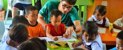 A Projects Abroad volunteer working with children in the Philippines sits with a group of kindergarten children in a classroom during his Childcare Project. 